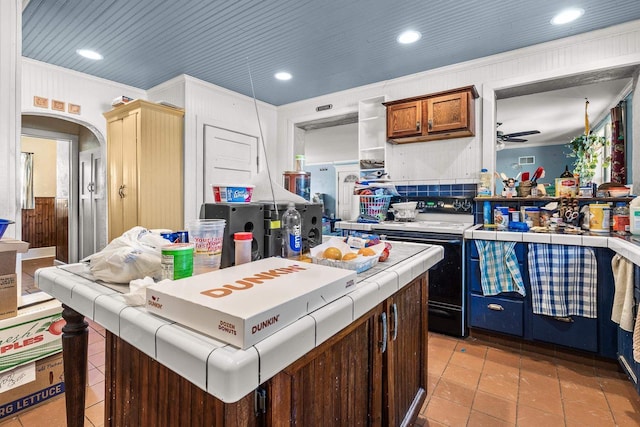 kitchen with ceiling fan, a center island, black electric range oven, tile countertops, and crown molding