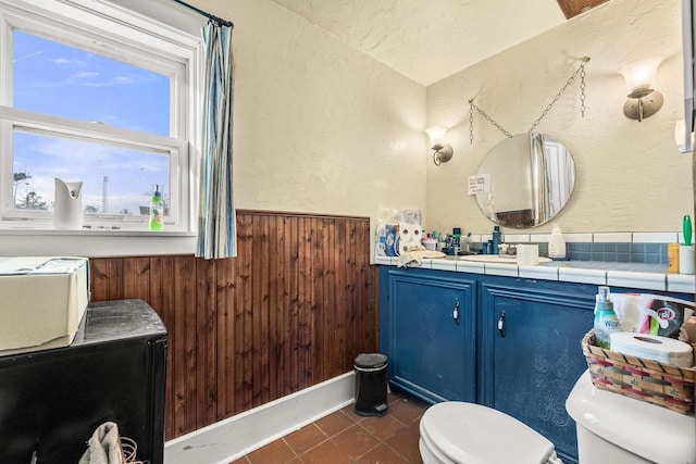 bathroom featuring tile patterned floors, wooden walls, vanity, and toilet