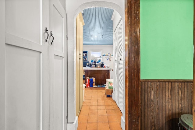 hall featuring light tile patterned flooring and wooden walls