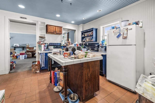 kitchen featuring a center island, white refrigerator, ornamental molding, light tile patterned floors, and tile counters