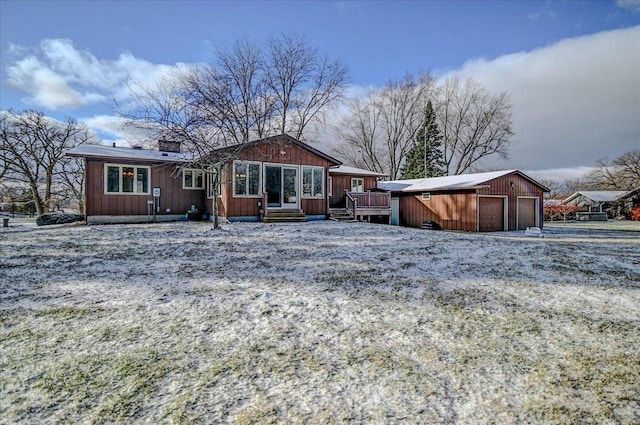 snow covered rear of property with a deck, an outdoor structure, and a garage