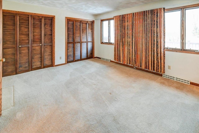 unfurnished bedroom with a textured ceiling, carpet floors, and two closets