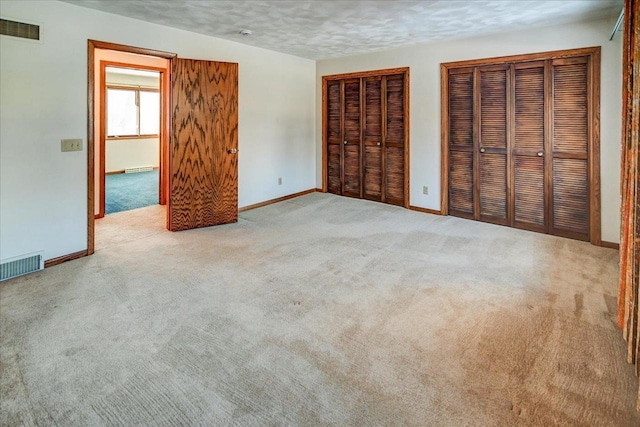 unfurnished bedroom with a textured ceiling, carpet floors, and two closets