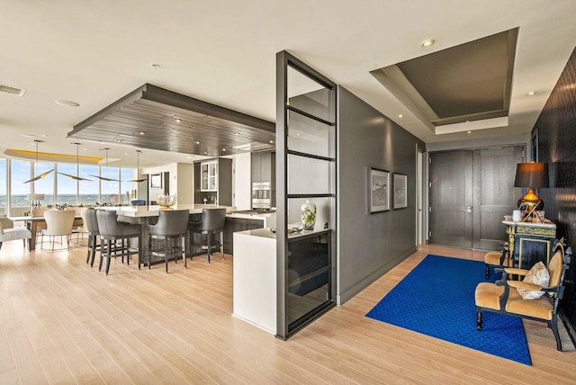 interior space with pendant lighting, light hardwood / wood-style floors, a raised ceiling, and a kitchen breakfast bar