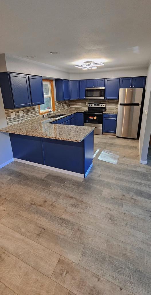 kitchen featuring light hardwood / wood-style flooring, blue cabinets, backsplash, kitchen peninsula, and appliances with stainless steel finishes