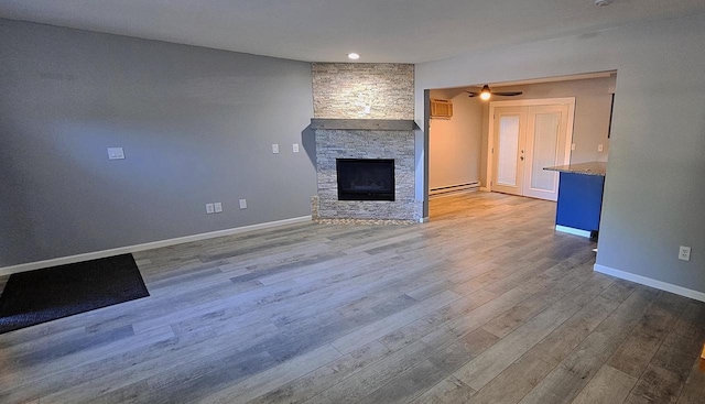 unfurnished living room with baseboard heating, a stone fireplace, ceiling fan, and light hardwood / wood-style floors