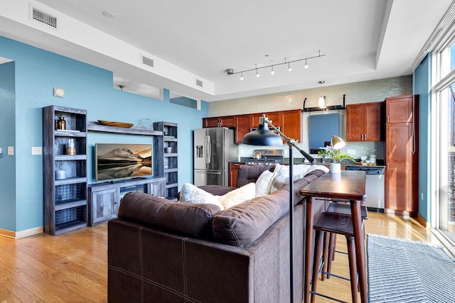 living room featuring a tray ceiling, light hardwood / wood-style flooring, and track lighting