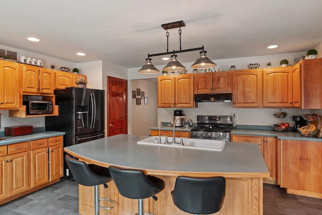 kitchen featuring stainless steel gas range oven, black fridge with ice dispenser, sink, decorative light fixtures, and a center island with sink