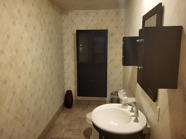 bathroom featuring a sink, baseboards, toilet, and stone finish floor