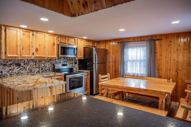 kitchen with wooden walls, sink, light stone countertops, and appliances with stainless steel finishes