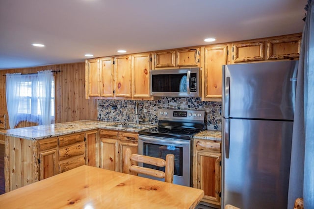 kitchen featuring light stone countertops, appliances with stainless steel finishes, backsplash, light brown cabinetry, and wood walls