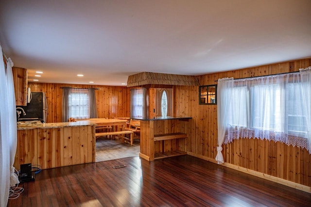 kitchen featuring kitchen peninsula, wood walls, black refrigerator, and dark hardwood / wood-style floors