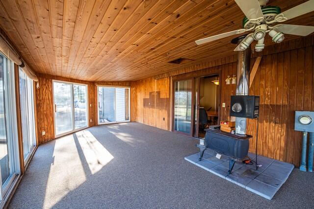 unfurnished sunroom with a wood stove, wooden ceiling, ceiling fan, and a healthy amount of sunlight