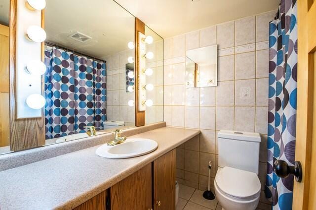 bathroom with tile patterned floors, vanity, toilet, and tile walls