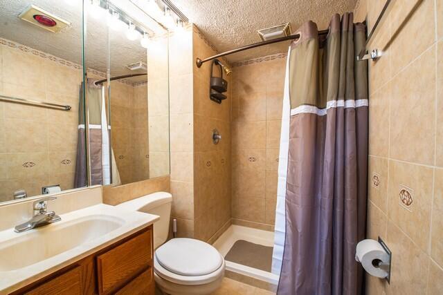 bathroom with a shower with curtain, tile patterned floors, a textured ceiling, toilet, and vanity