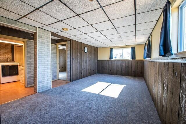 spare room with a paneled ceiling, carpet floors, and wooden walls