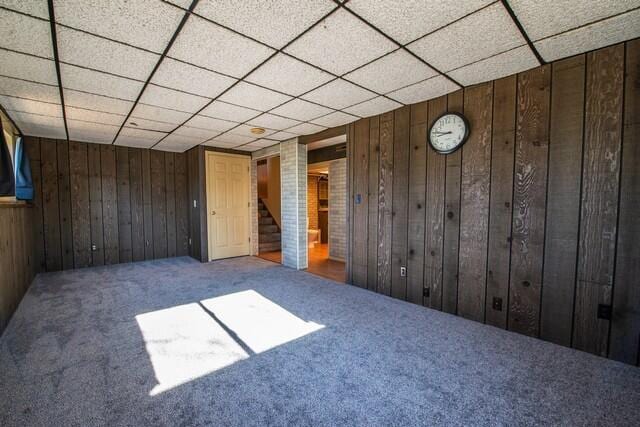 unfurnished room with carpet flooring, a paneled ceiling, and wood walls