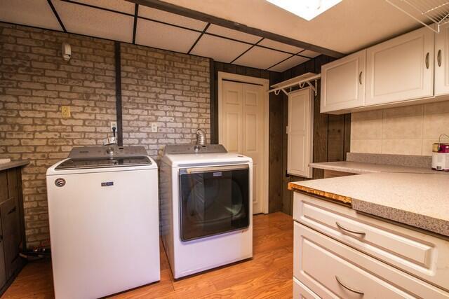 clothes washing area featuring washer and dryer, cabinets, brick wall, and light hardwood / wood-style flooring