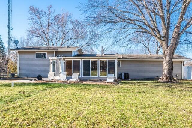 rear view of property with a sunroom, a lawn, and central AC