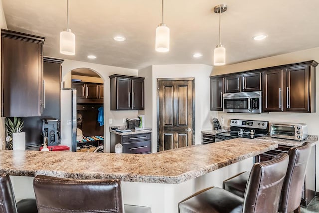 kitchen with a kitchen bar, pendant lighting, stainless steel appliances, and dark brown cabinets