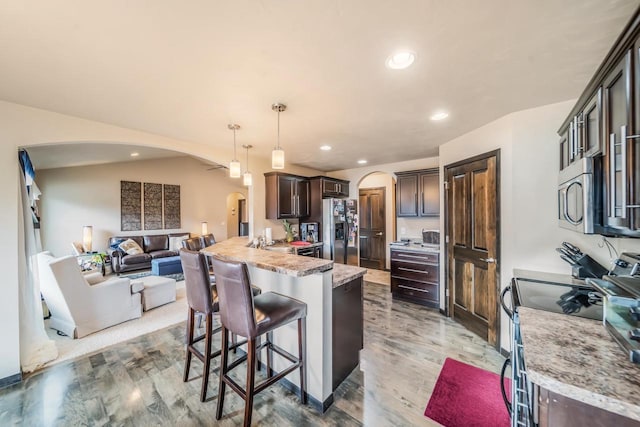 kitchen with dark brown cabinetry, stainless steel appliances, light hardwood / wood-style flooring, vaulted ceiling, and decorative light fixtures