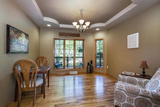 living area featuring a chandelier, light hardwood / wood-style flooring, and a raised ceiling