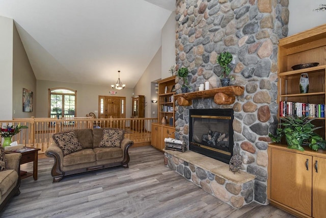 living room featuring light hardwood / wood-style floors, a stone fireplace, high vaulted ceiling, and a chandelier