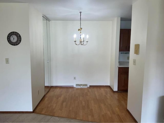 unfurnished dining area featuring an inviting chandelier and hardwood / wood-style flooring