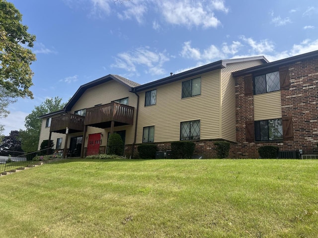 back of house with central air condition unit, a balcony, and a lawn