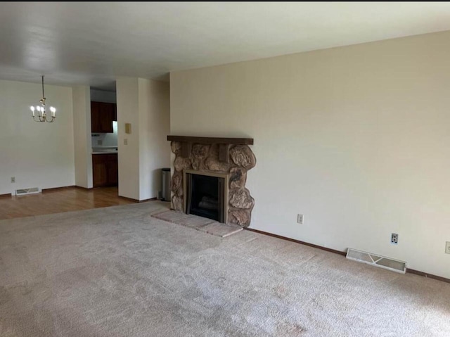 unfurnished living room featuring carpet, a stone fireplace, and an inviting chandelier