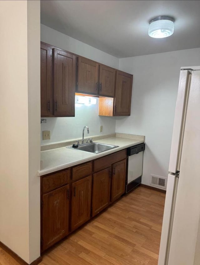 kitchen featuring white appliances, light hardwood / wood-style flooring, dark brown cabinetry, and sink