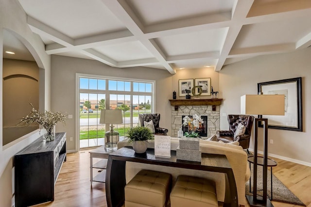 interior space with beamed ceiling, light hardwood / wood-style floors, a stone fireplace, and coffered ceiling