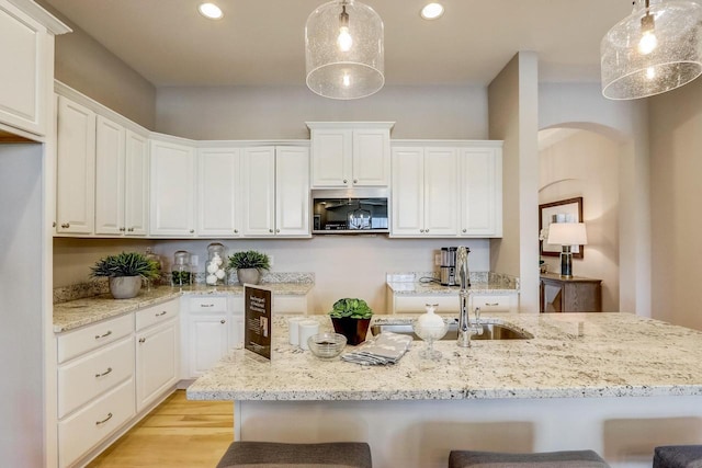 kitchen with light stone countertops, light hardwood / wood-style flooring, white cabinets, and decorative light fixtures