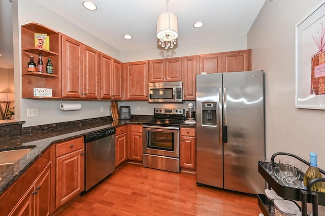 kitchen with appliances with stainless steel finishes, light wood-type flooring, decorative light fixtures, and dark stone countertops