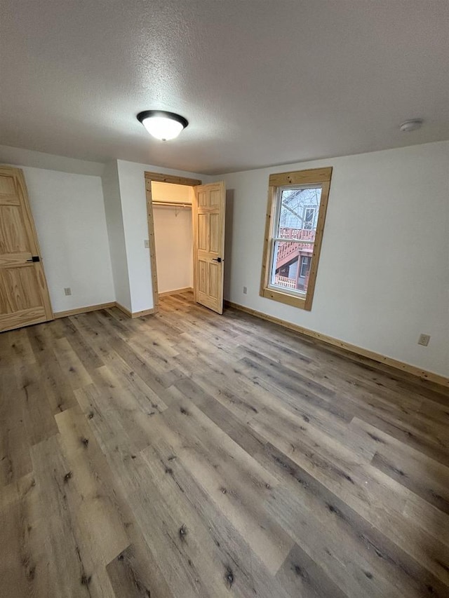 unfurnished bedroom with hardwood / wood-style floors, a walk in closet, a textured ceiling, and a closet