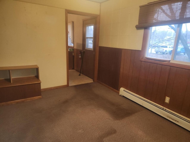 empty room featuring wood walls, carpet floors, and a baseboard heating unit