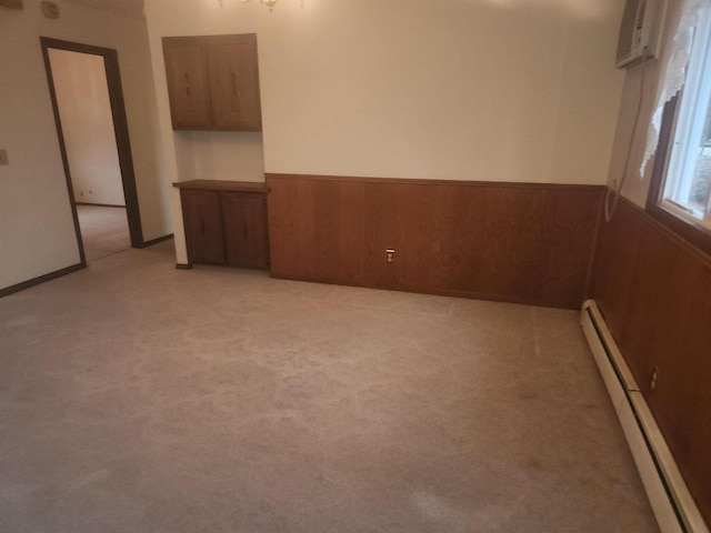 empty room with a baseboard radiator, light colored carpet, and wood walls