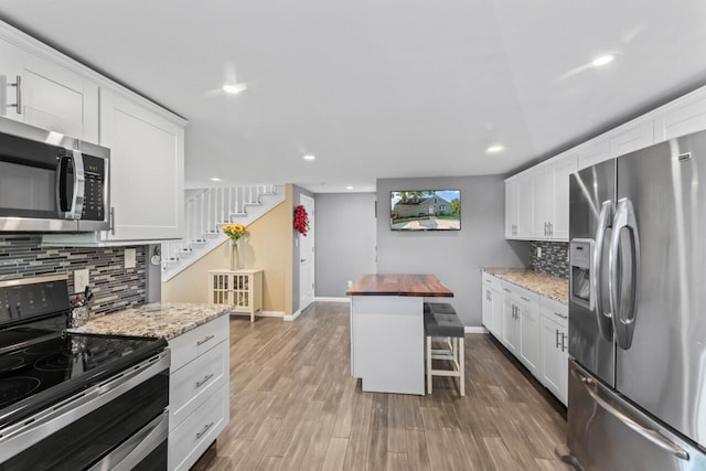 kitchen with white cabinetry, a kitchen breakfast bar, light stone counters, light hardwood / wood-style flooring, and appliances with stainless steel finishes