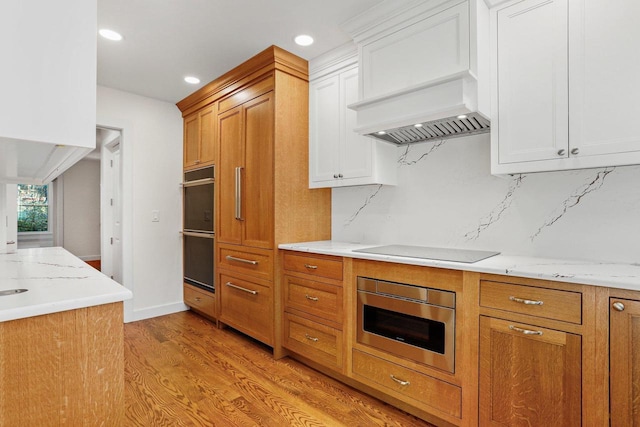 kitchen featuring white cabinetry, black electric stovetop, light hardwood / wood-style floors, and multiple ovens