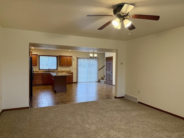 kitchen featuring carpet flooring, black refrigerator, ceiling fan with notable chandelier, a kitchen island, and hanging light fixtures