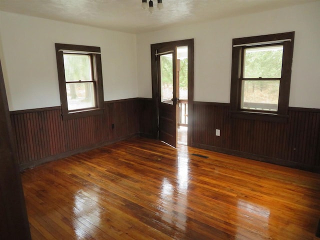 spare room featuring a textured ceiling, wooden walls, a wealth of natural light, and dark wood-type flooring