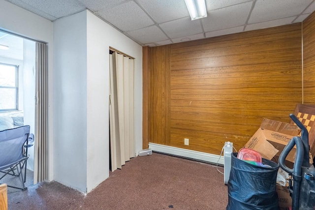 interior space with carpet flooring, a paneled ceiling, and wooden walls