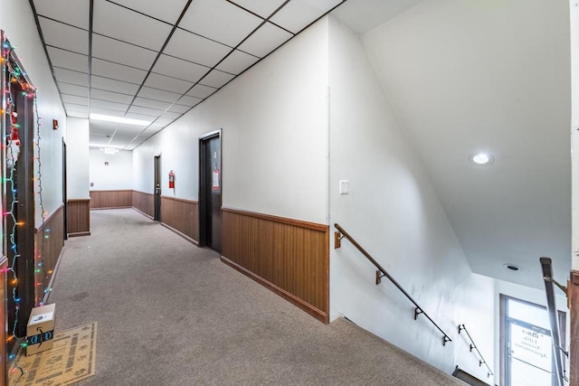 hallway featuring a paneled ceiling, wood walls, and light colored carpet