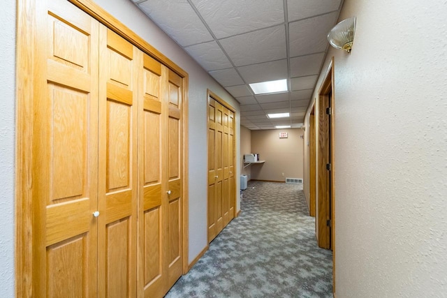 hall with a paneled ceiling and carpet