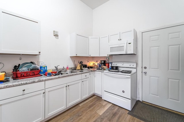 kitchen with white cabinetry, light hardwood / wood-style flooring, light stone countertops, and white appliances