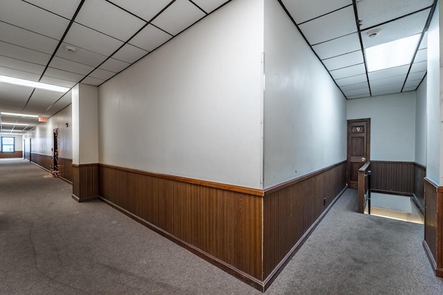 corridor with dark colored carpet, a paneled ceiling, and wood walls