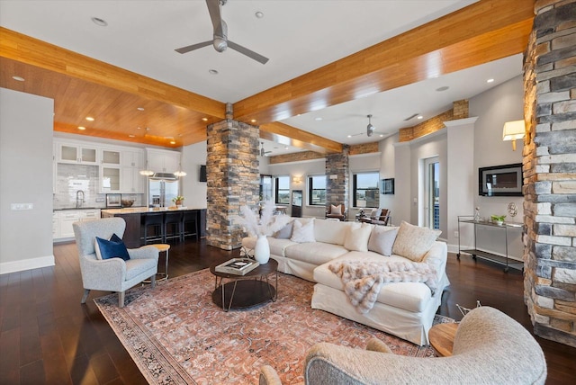 living room featuring dark wood-type flooring, sink, ceiling fan, beamed ceiling, and decorative columns