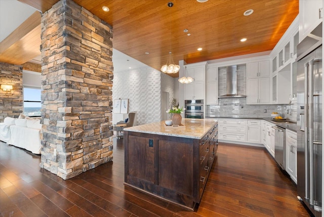 kitchen with white cabinets, wall chimney exhaust hood, a kitchen island, dark hardwood / wood-style flooring, and stainless steel appliances