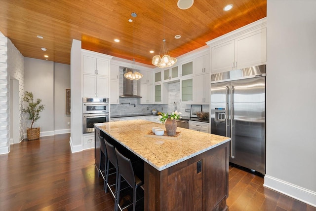 kitchen featuring white cabinetry, wall chimney range hood, dark hardwood / wood-style flooring, a kitchen island, and appliances with stainless steel finishes