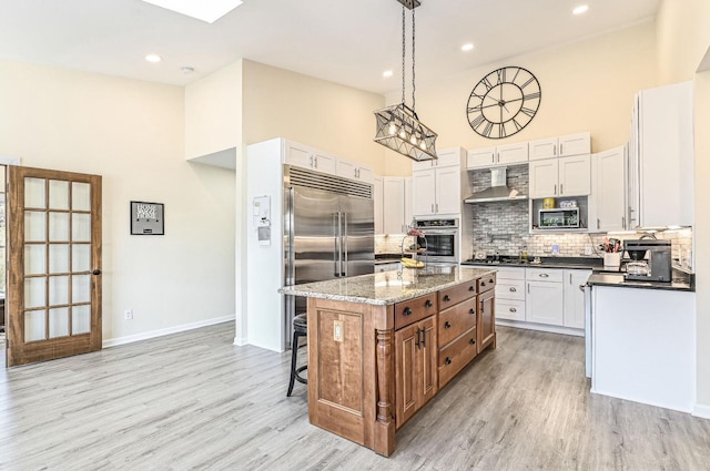 7134 N Tichigan Rd, Waterford, WI 53185 - kitchen with appliances with stainless steel finishes, high vaulted ceiling, wall chimney exhaust hood, a kitchen island, and decorative backsplash